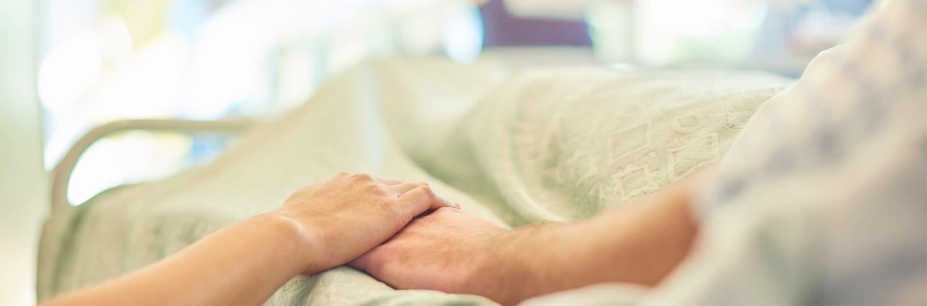 Holding hands with a patient in a hospital bed