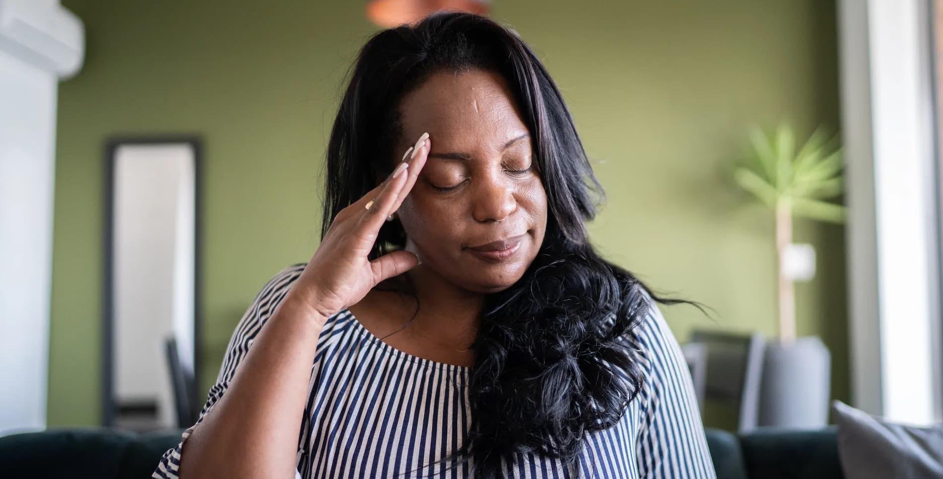 A woman with closed eyes clutches her head with one hand