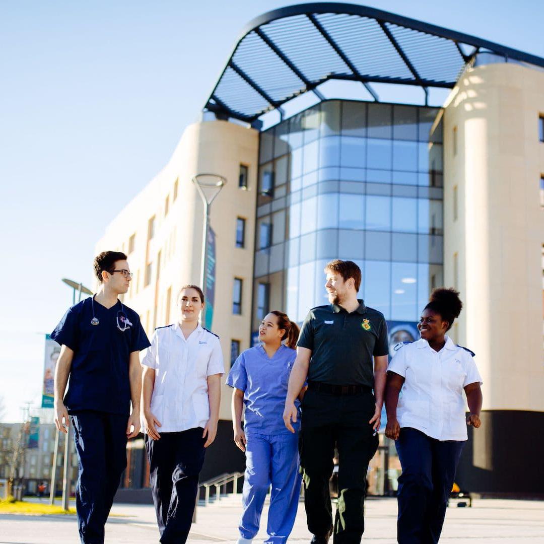 A group of health students in various uniforms walking in front of the Allam Medical Building