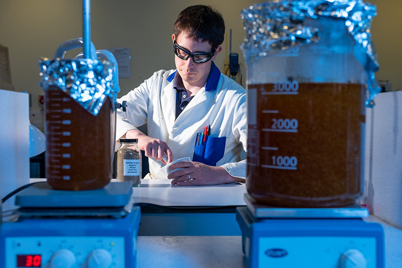 Image of Dr Martin Taylor grinding samples, with two glass beakers bubble in the foreground