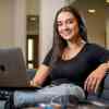 Hull Philosophy student, Mayla Singh, smiling to the camera while working on a laptop in the Brynmor Jones Library.